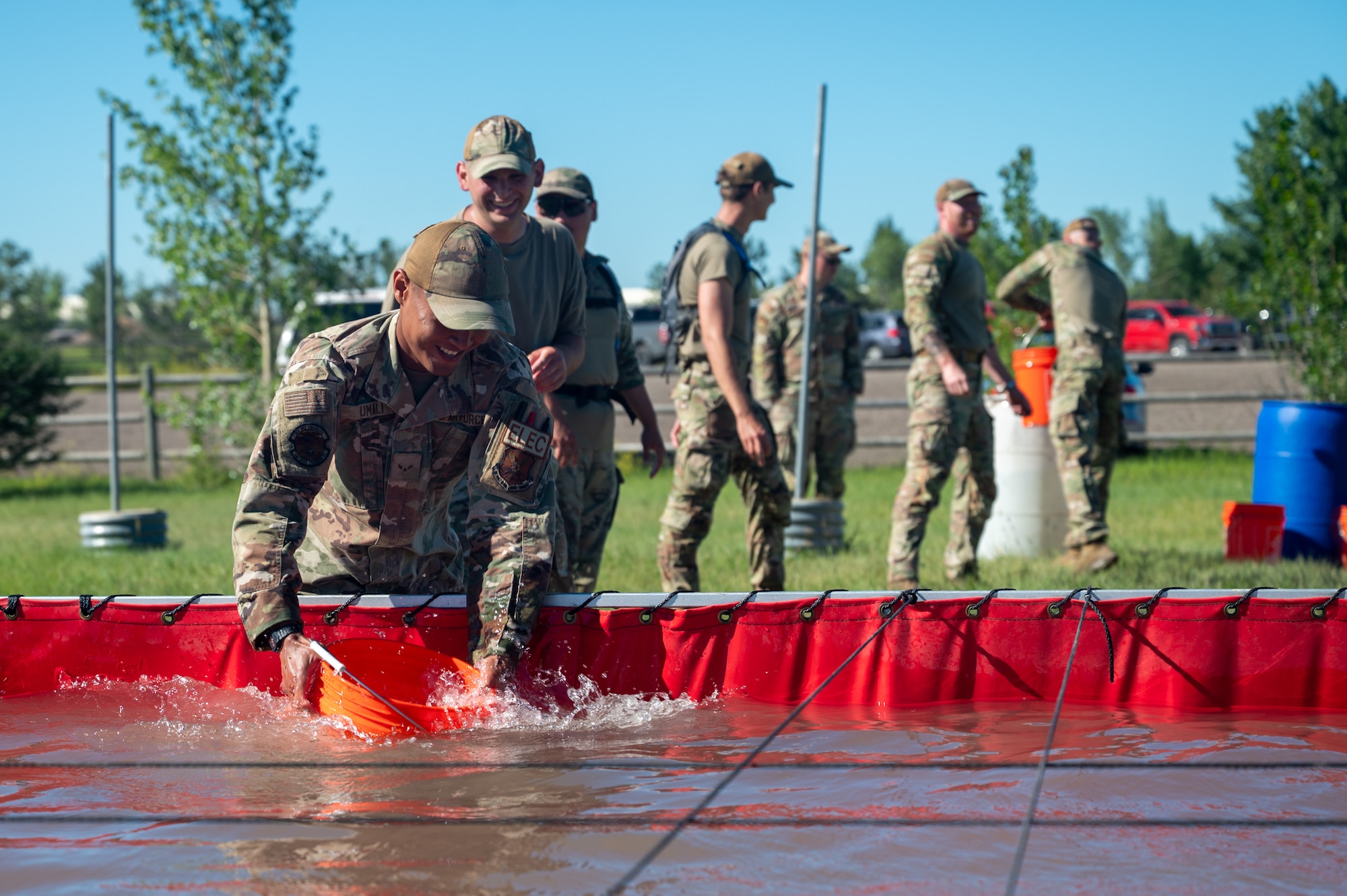 A uniformed Airman smiles while collecting water with a bucket.