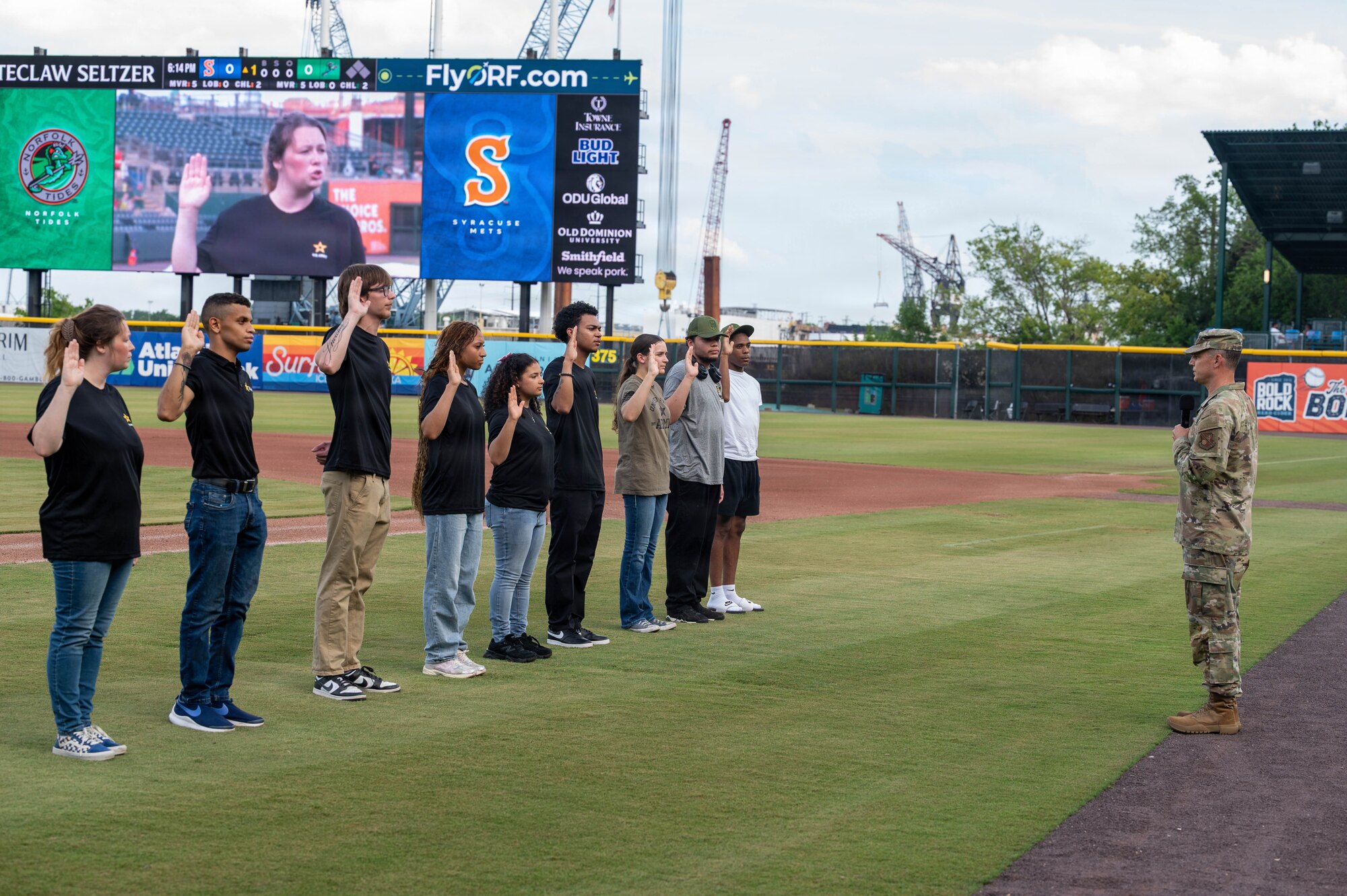 A group of people raise their right hand at a baseball field.