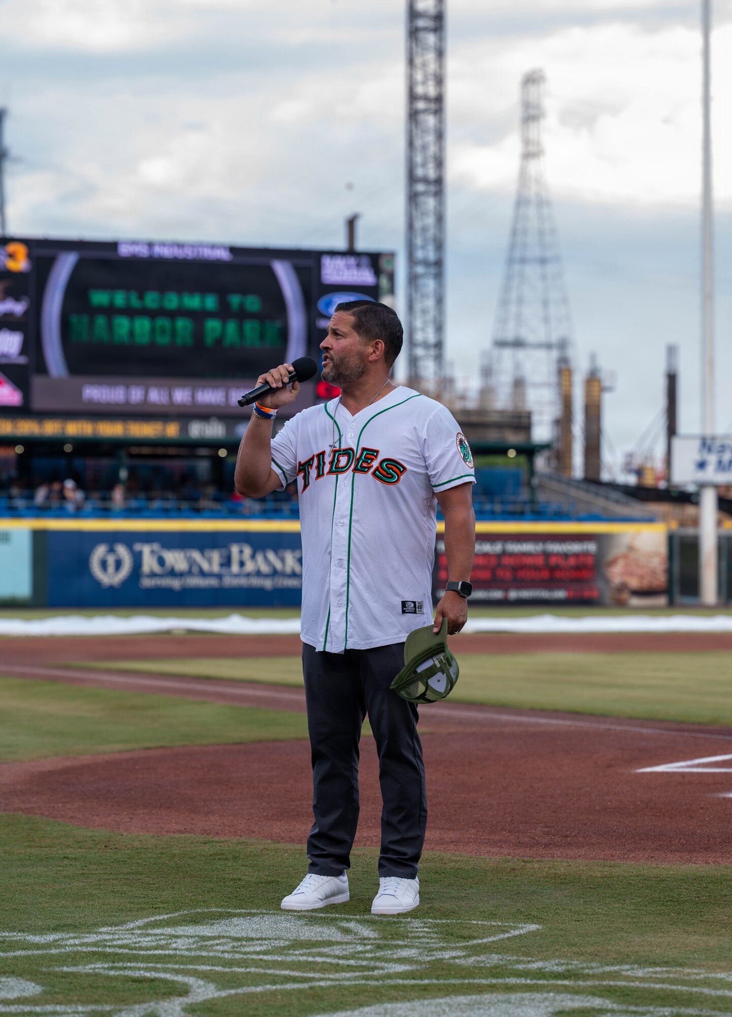 A man holds a microphone at a baseball field.