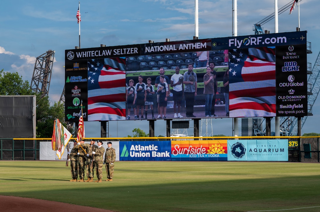 A group of Soldiers holds flags at a baseball field.