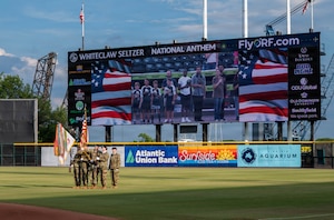 A group of Soldiers holds flags at a baseball field.