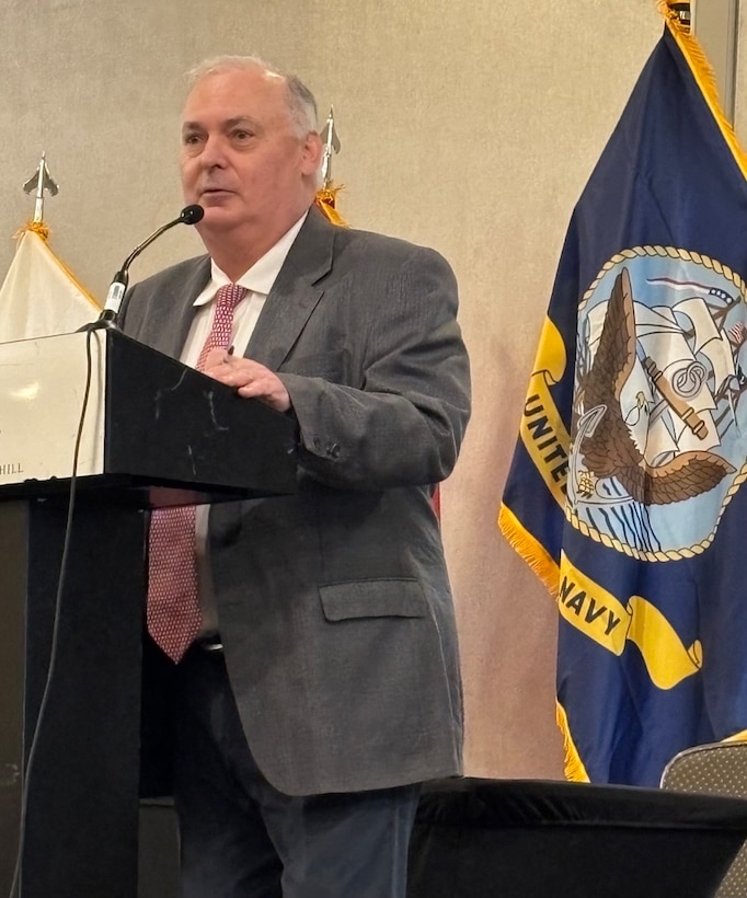 Man in suit speak at podium in front of flags.