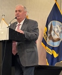 Man in suit speak at podium in front of flags.
