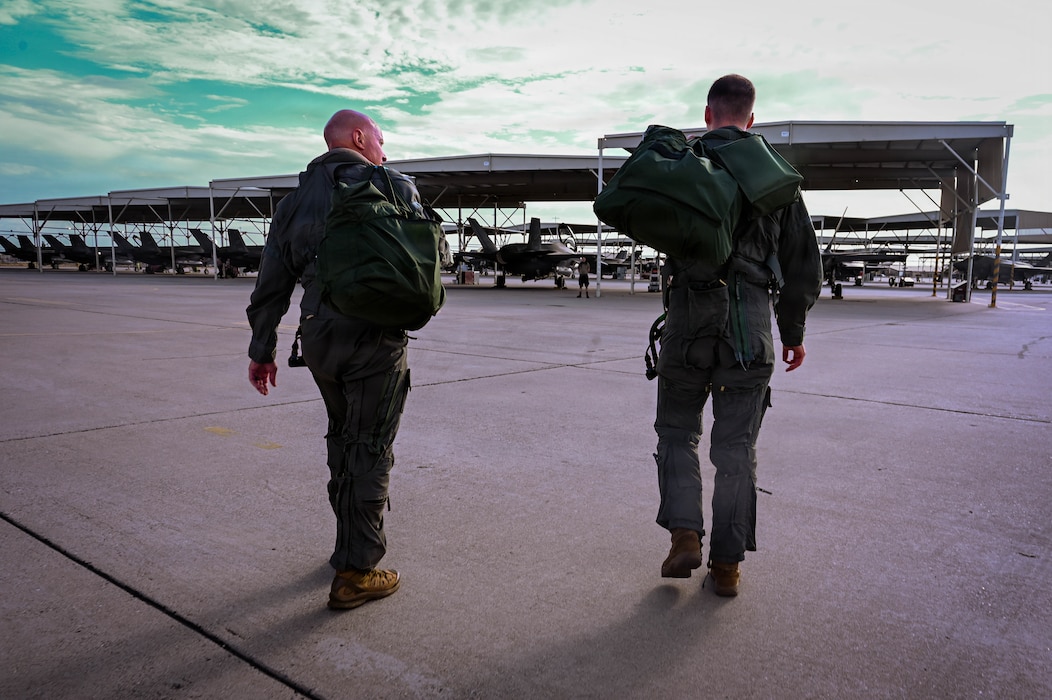Two U.S. Airmen walk out onto a flightline.