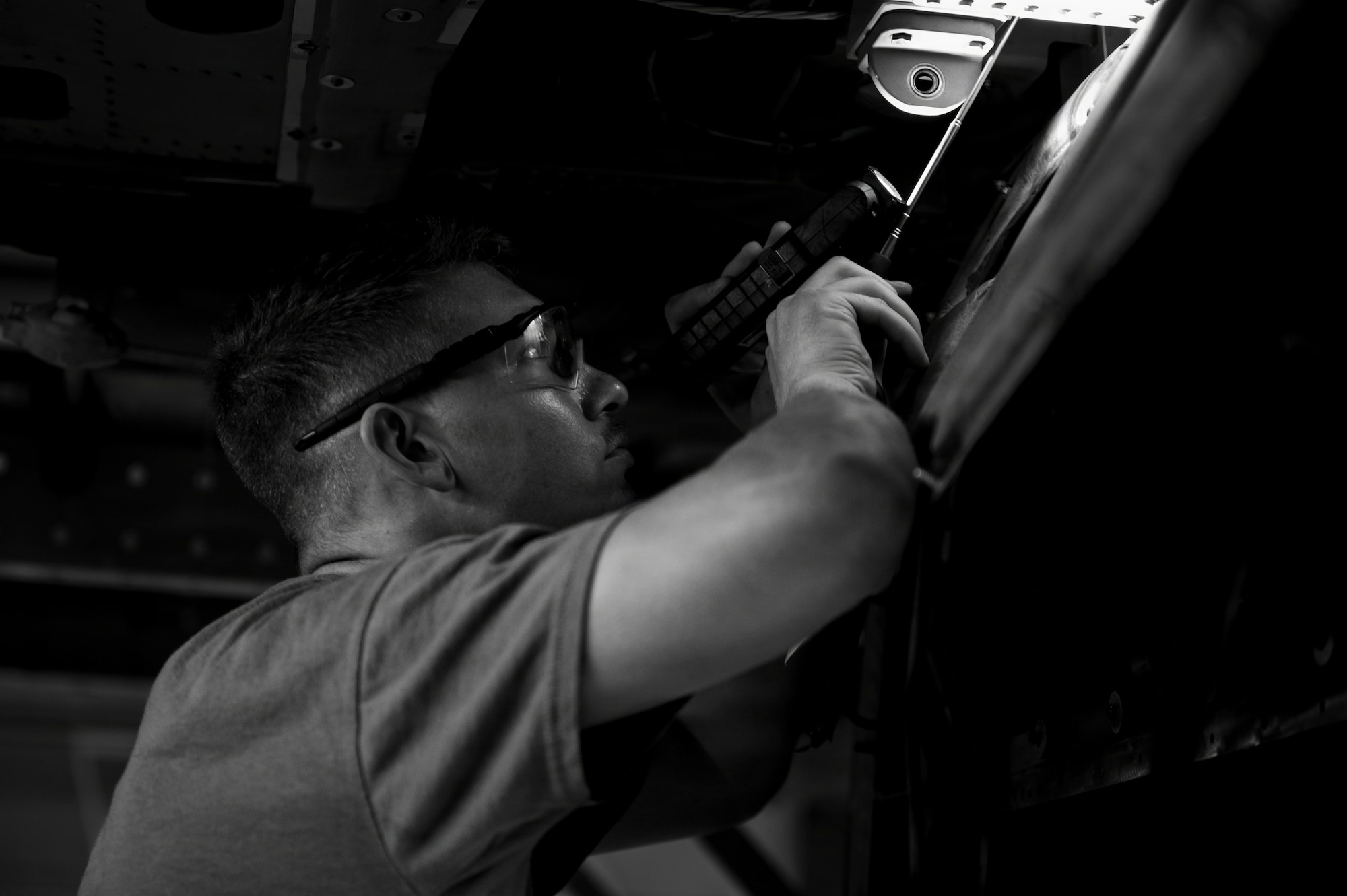 A man uses a flashlight to see where he is working on the inside of a helicopter.