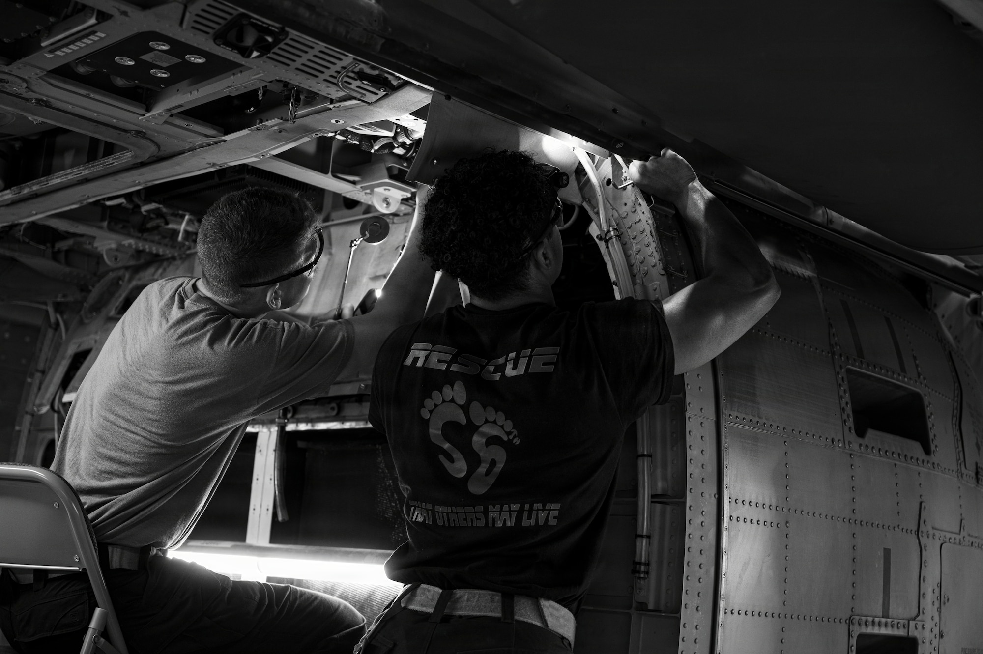 Two men perform maintenance inside a helicopter.