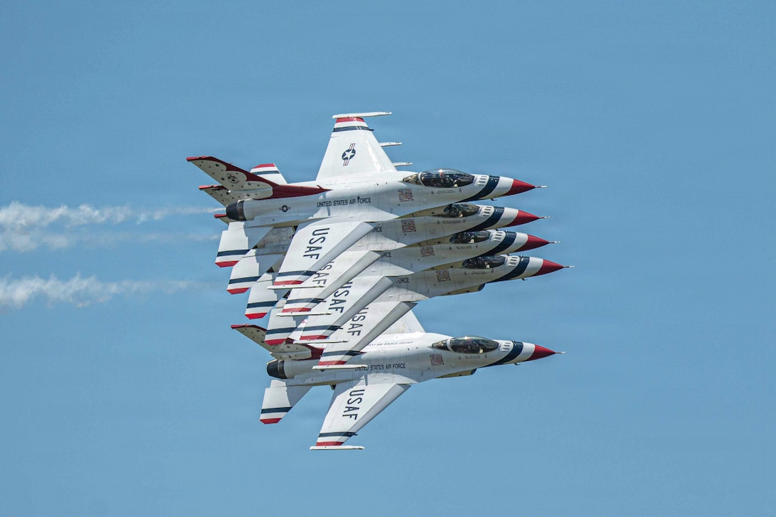 Five identical aircraft fly diagonally on top of one another in a blue sky.