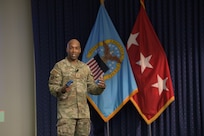 Air Force Chief Master Sgt. Kenneth Bruce speaks on a stage in front of a DLA flag and a three-star flag