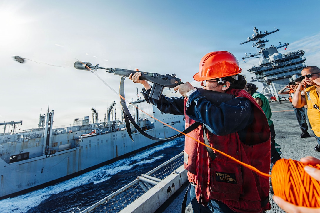 A person standing on the deck of a ship fires a shot line toward another vessel at sea.