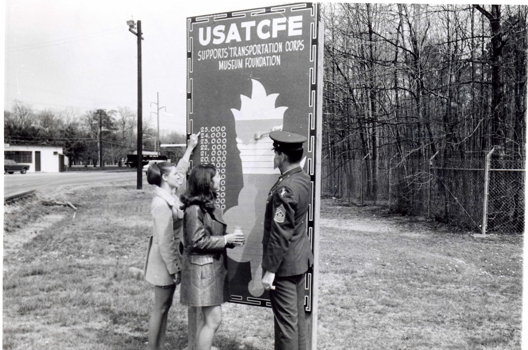 Mrs. Sprouse and Mrs. Leonard assist Transportation School Command Sergeant Major Jeffress updated the Transportation Museum fundraising board by the Fort Eustis gate in 1971. (Courtesy photo from U.S. Army Transportation Museum Photo Collection)