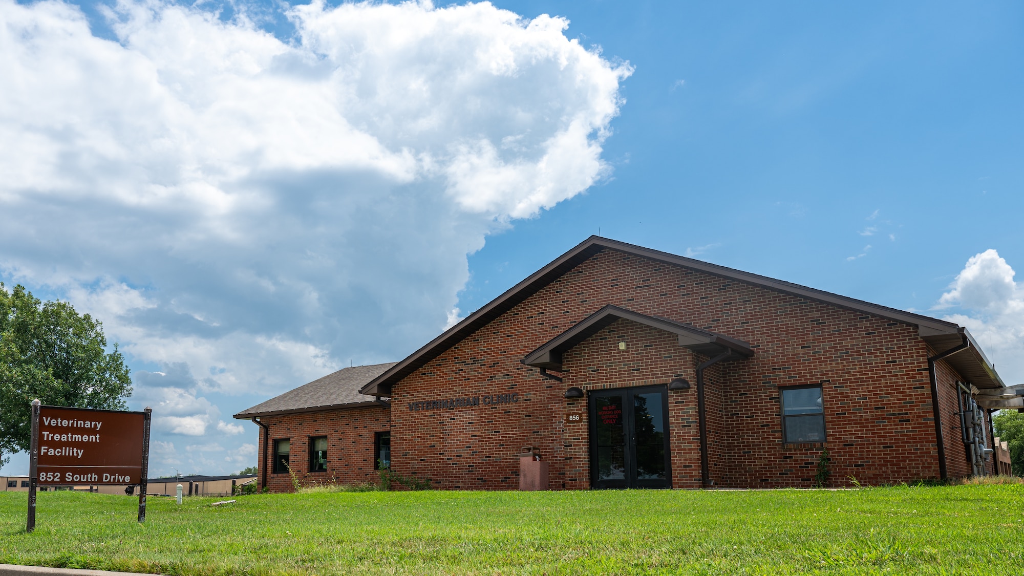A brown brick building at the top of a slight hill. The sky is blue with some clouds coming in on the left.