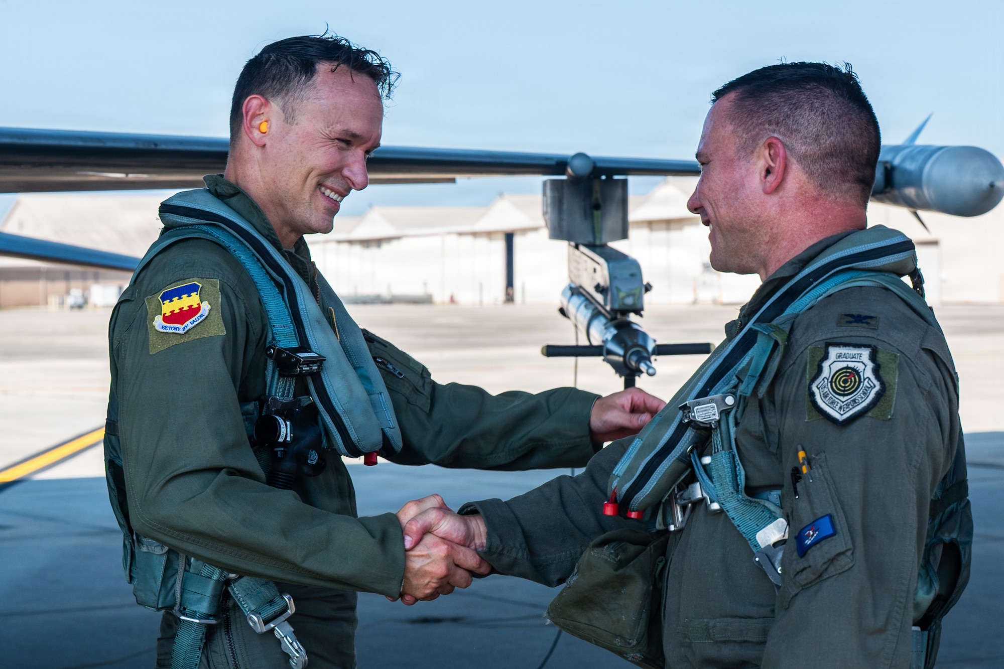 Two Airmen wearing flight suits shake hands