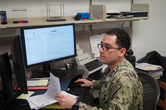 Hospital Corpsman 3rd Class Nicolas  Pantoja, assigned to Navy Medicine Readiness and Training Command Rota, reviews overseas screening documentation as the Overseas Screening and Exceptional Family Member Program coordinator at Naval Station Rota, Spain, May 10, 2025. Pantoja helps ensure service members and their families are medically prepared for overseas assignments, supporting operational readiness throughout the European and African areas of responsibility. (U.S. Navy photo by Lt. Cmdr. Alicia Sacks)