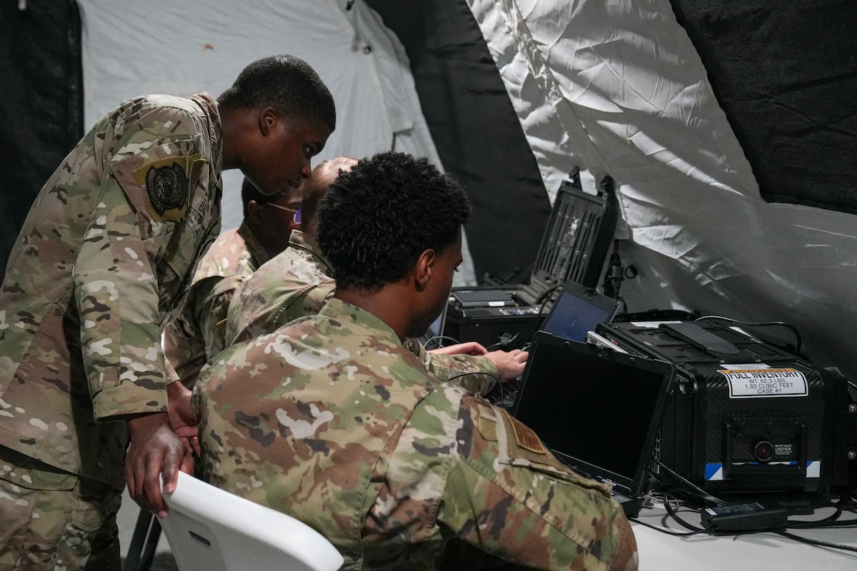 an airman looks over the shoulder of another airman as they look at a computer