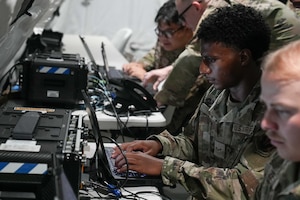An Airman looks at a laptop in front of a deployable comms kit