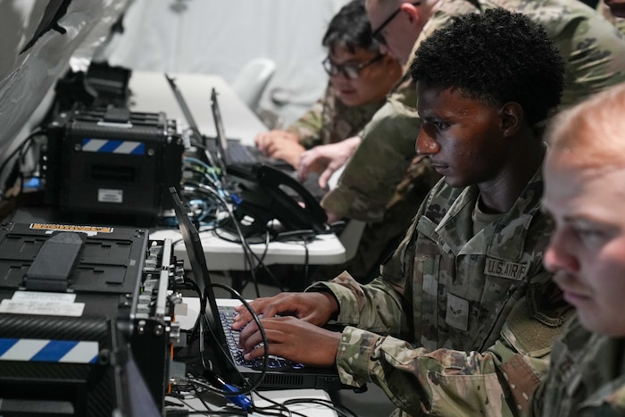 An Airman looks at a laptop in front of a deployable comms kit