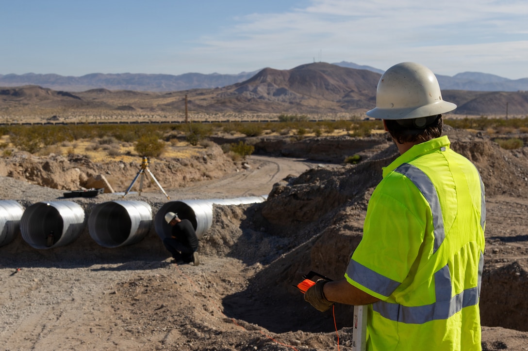Personnel with the Base Maintenance and Engineering Department work to repair a washed-out section of Range Road aboard Marine Corps Logistics Base Barstow, California, July 14. The road, which was severely damaged by heavy rains in September 2025, is being reconstructed with a Type II aggregate base, reinforced retaining walls, and 3-foot concrete Sonotubes designed to divert runoff and prevent future washouts. The reconstruction project is slated for completion in mid-August 2026, restoring safe and reliable vehicular access to the base training ranges for Marines and civilian personnel.
