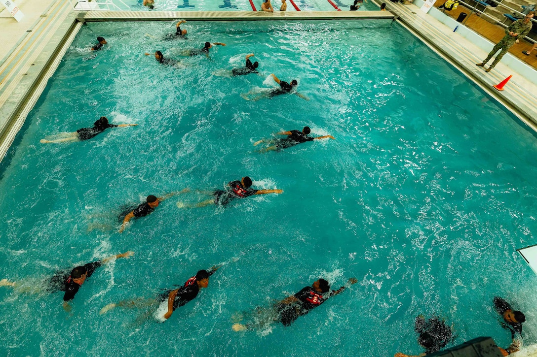 People wearing T-shirts and shorts swim freestyle in a pool that doesn't have lanes.