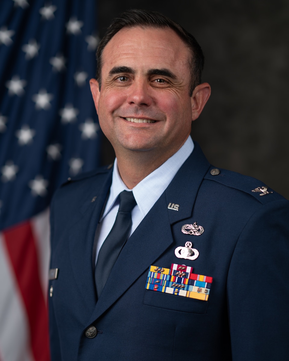 A standard U.S. Air Force biography photo showcasing a head and shoulders portrait of U.S. Air National Guard Col. Michael Baird in a head and shoulders portrait, positioned in a 45 degree view with his official dress uniform with a U.S. flag affixed behind his right shoulder.