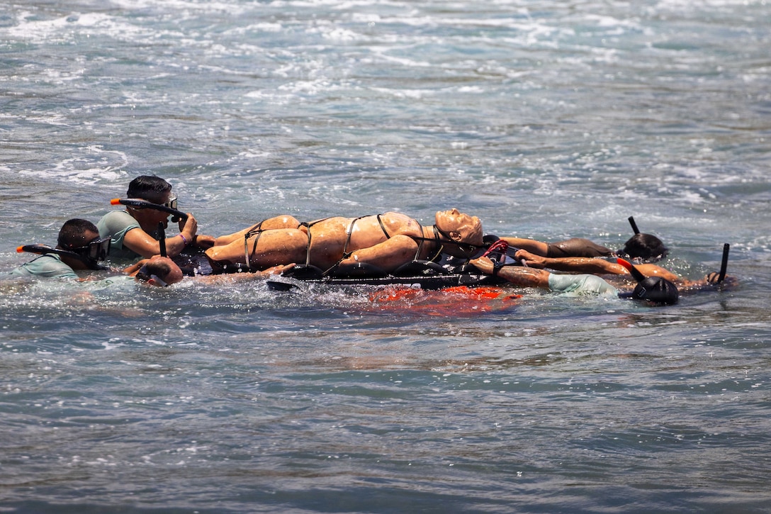 U.S. and partner nation rescue personnel swim with snorkeling gear while towing a floating rescue litter with a mannequin during the day.