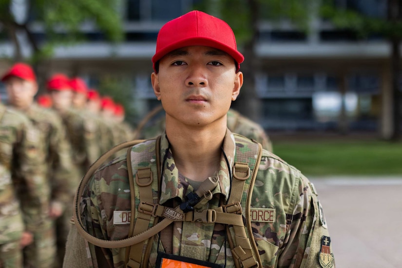 A man wearing a camouflage military uniform and red hat stands at attention while in formation.