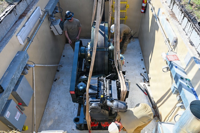 Airmen in a pit unstrap machinery from a crane
