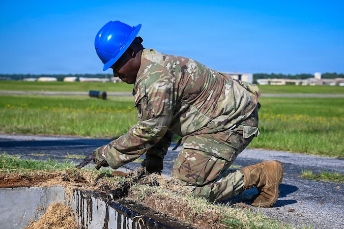 An Airman pulls grass and dirt away from the edge of a pit