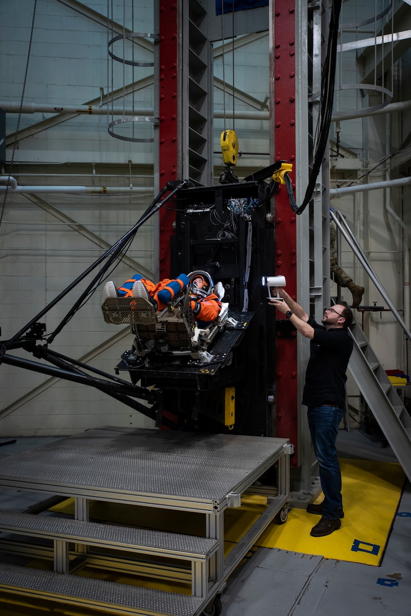 Max Grattan, right, Biodynamics Laboratory support contractor, conducts 3D surface scanning of a U.S. Air Force volunteer on the vertical deceleration tower at Wright-Patterson Air Force Base, Ohio, Nov. 3, 2023, to test the next replica of a seat and space suit for the Orion spacecraft. The Air Force Research Laboratory’s 711th Human Performance Wing sought active-duty military volunteers for an August 2026 collaborative study with NASA to evaluate the impact forces astronauts will face during future lunar landings. (U.S. Air Force photo / Richard Eldridge)