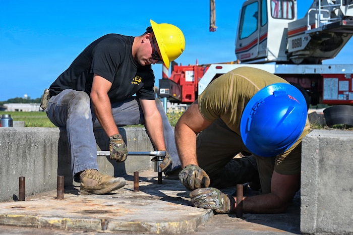 Two Airmen wearing hardhats tighten bolts
