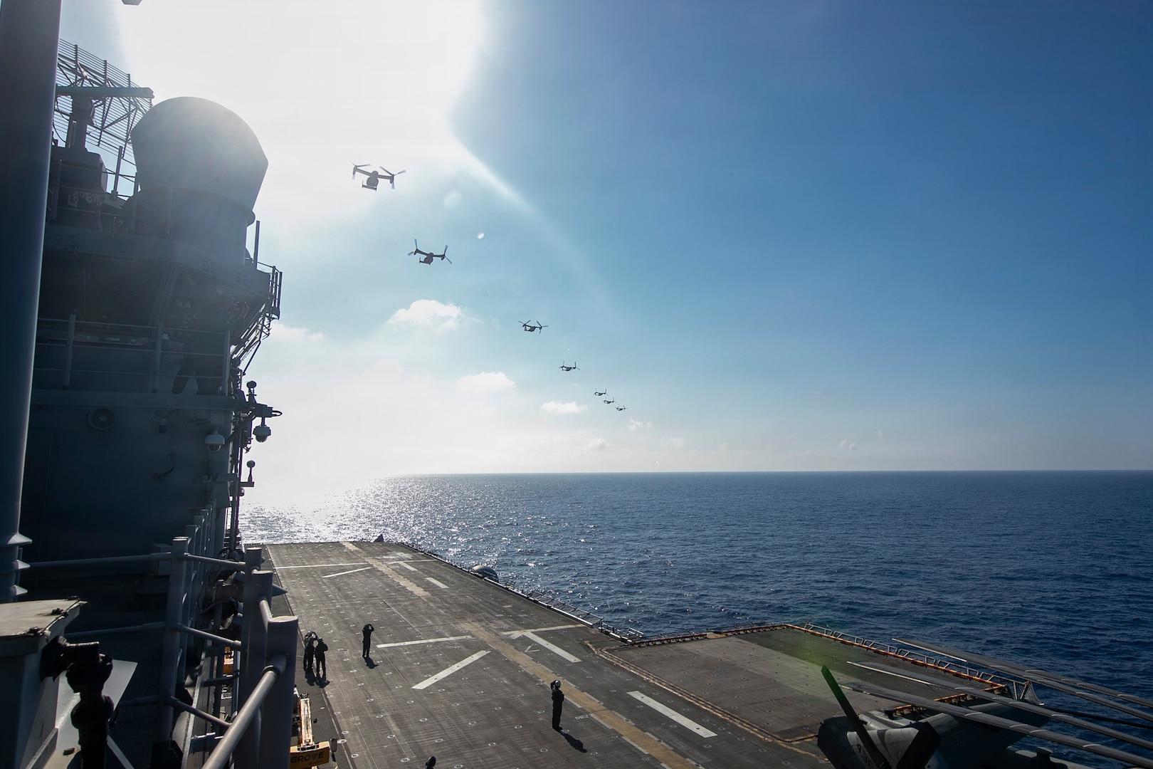 Seven military aircraft conduct a flyover of a Navy assault ship.