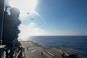 Seven military aircraft conduct a flyover of a Navy assault ship.
