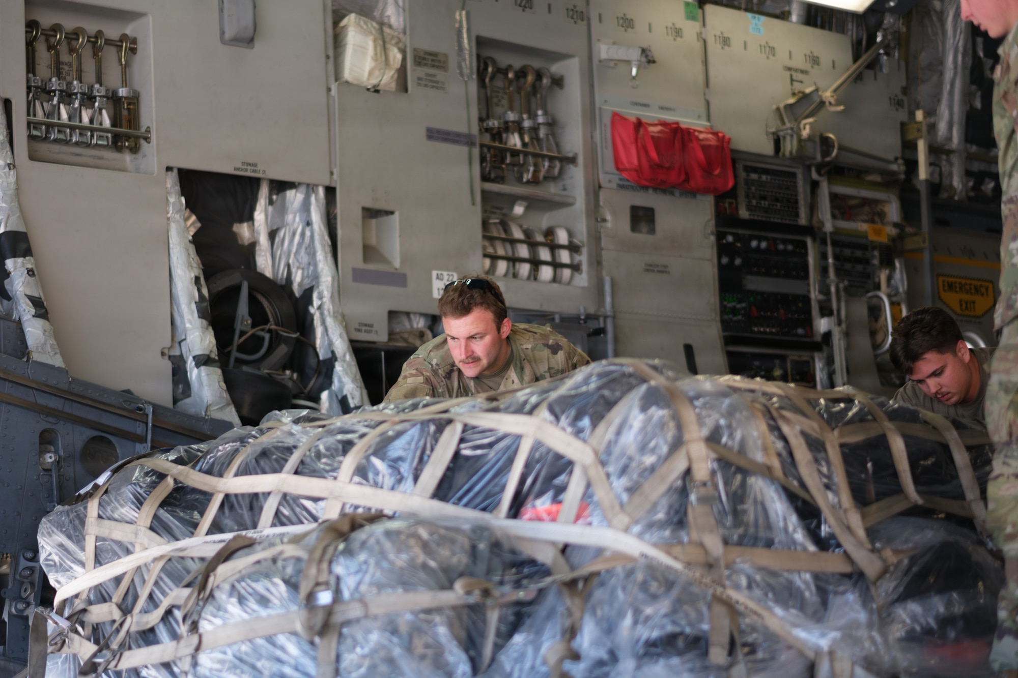 Airmen push a pallet of cargo off a cargo plane.