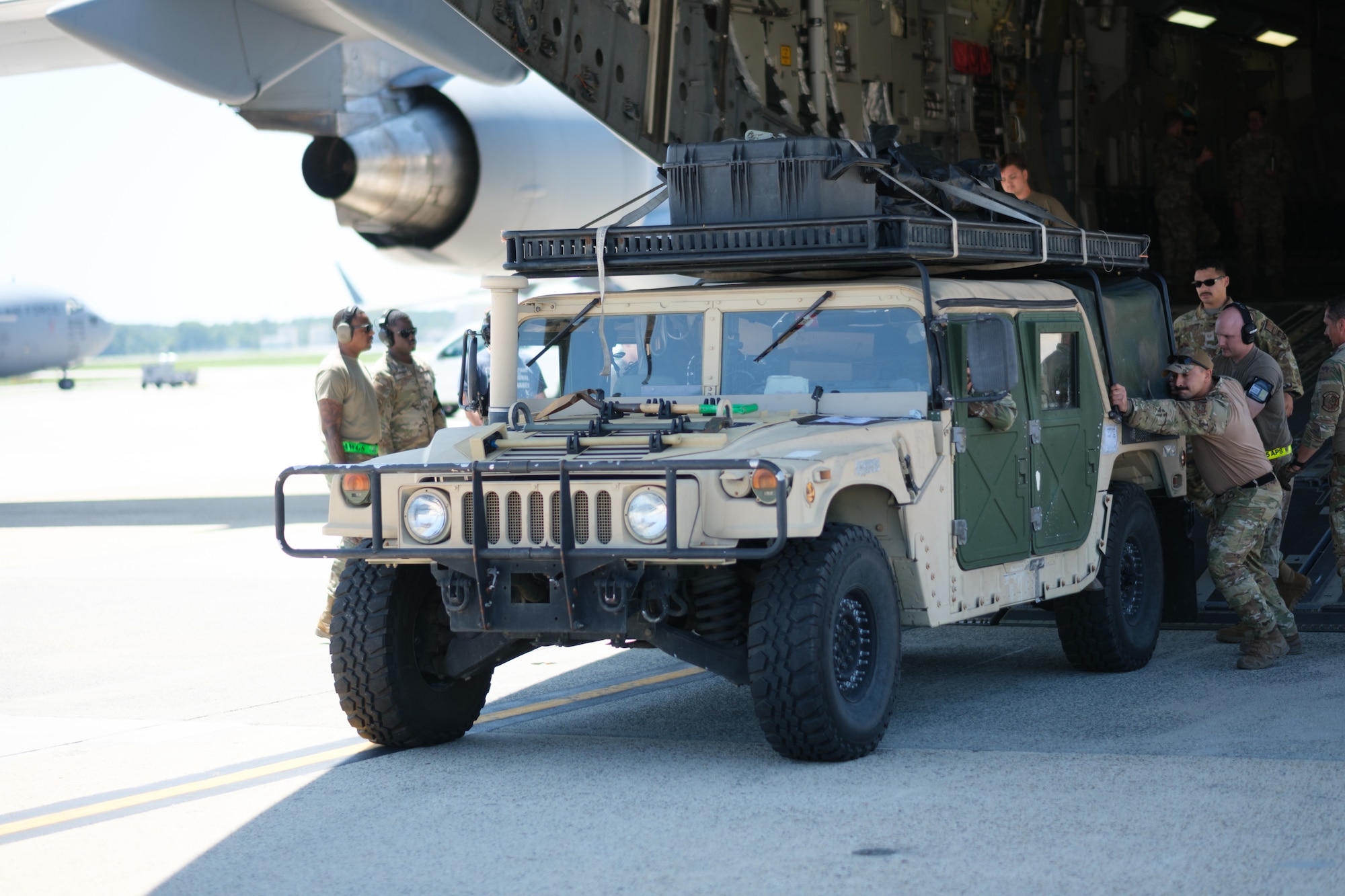 Airmen roll a military truck off a cargo plane.