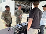Two soldiers speak with vendors at a drone event.