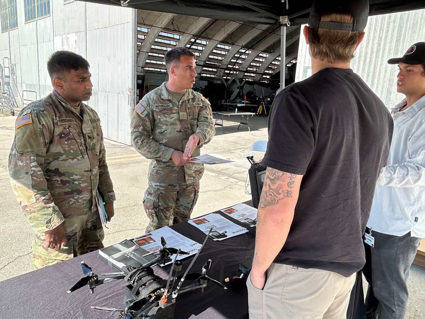 Two soldiers speak with vendors at a drone event.