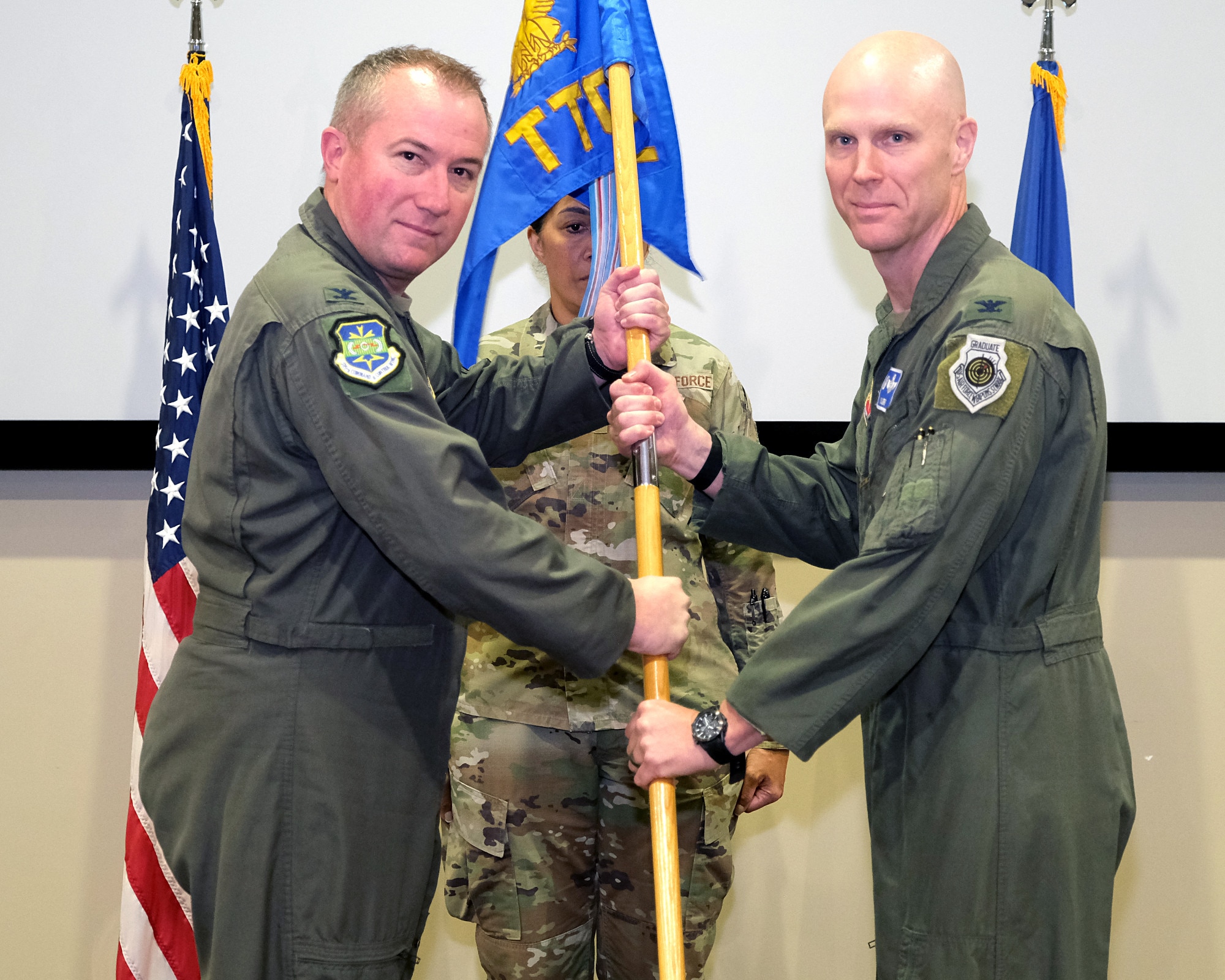 photo of three US Air Force Airman standing on a stage, two Airman are holding a unit flag.