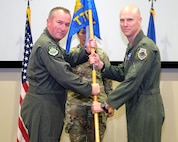 photo of three US Air Force Airman standing on a stage, two Airman are holding a unit flag.