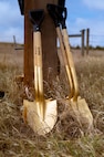 Image of shovels leaning against a fence post in a field.