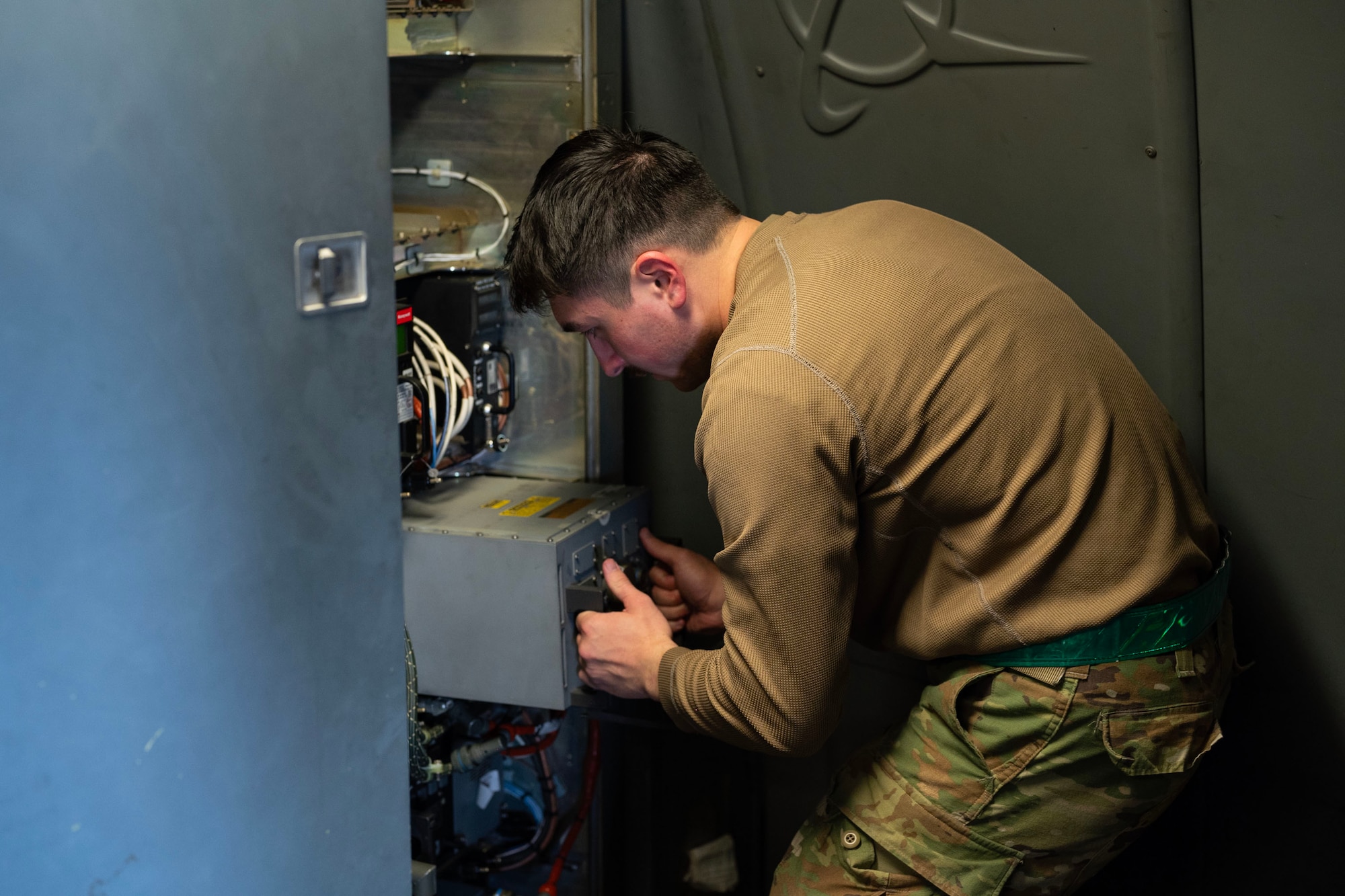 a medium shot of an airmen taking a cylinder out of a container with electrical wires sticking out, Airmen is in the right side of the frame from the waist up
