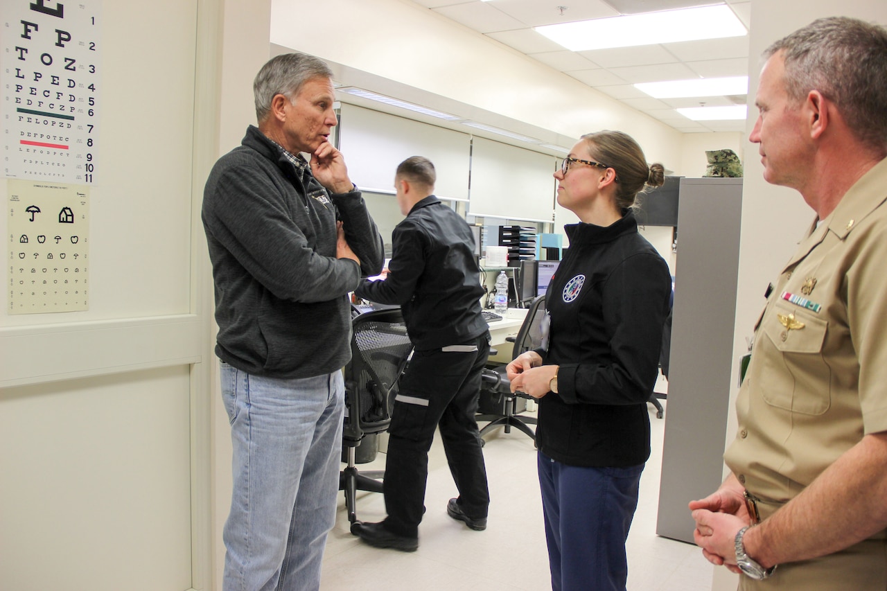 A man wearing casual attire speaks to a woman dressed in casual attire inside a medical facility.