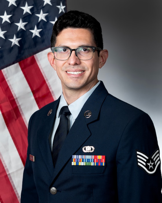 An airman in uniform poses in front of the U.S flag