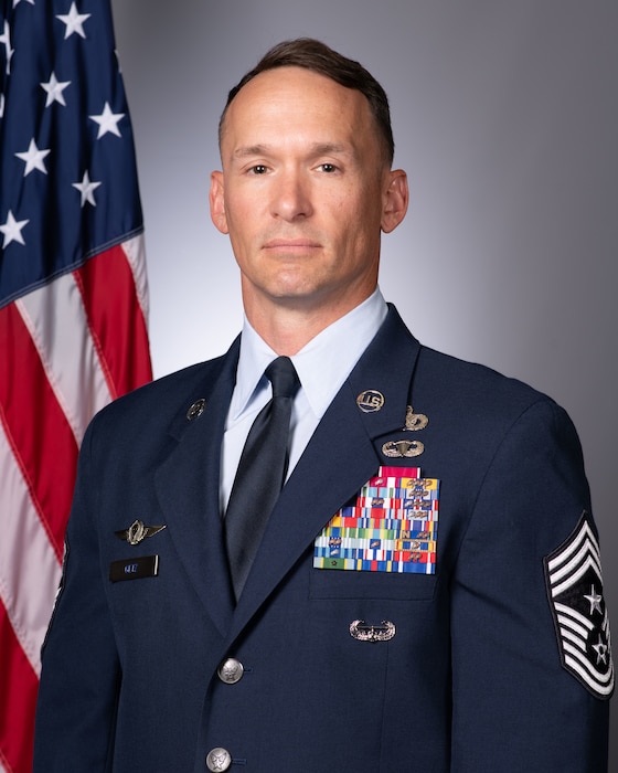 A Command Chief Master Sgt. poses for an official photo with the American flag to his left.