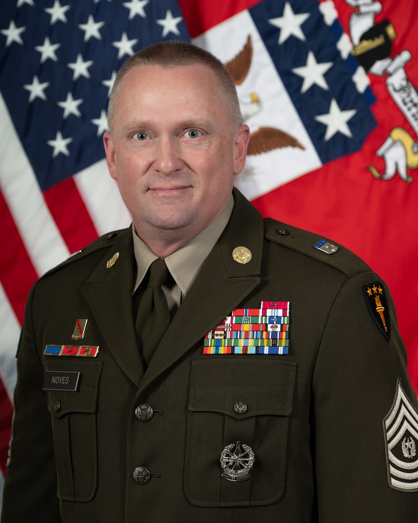 Photo of a man in front of two military flags.