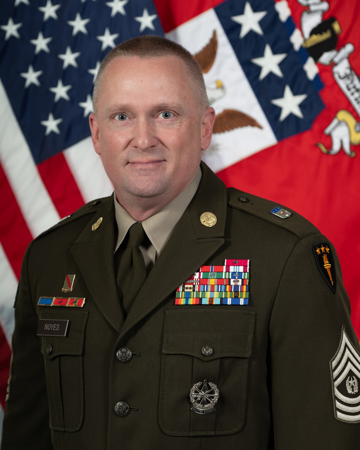 Photo of a man in front of two military flags.