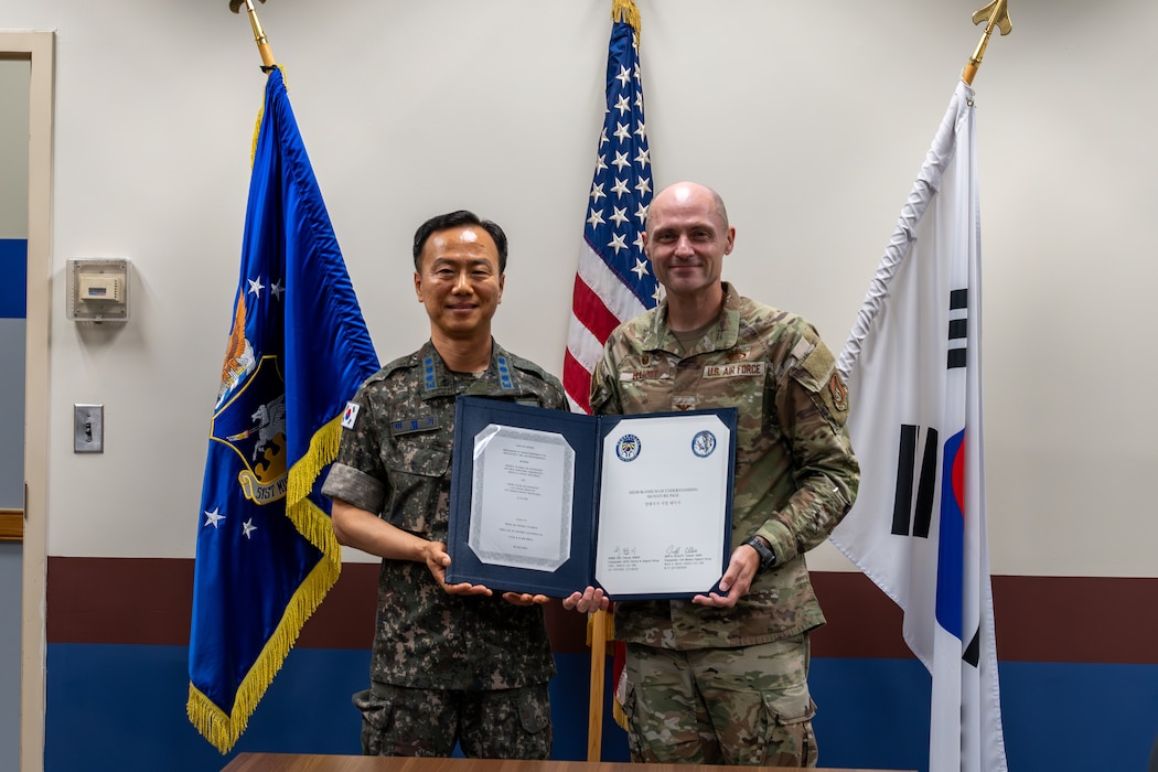 A USAF and ROKAF commander pose for a photo holding a signed memorandum.