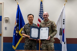 A USAF and ROKAF commander pose for a photo holding a signed memorandum.