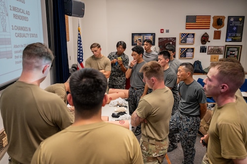 American and Japanese Airmen stand in a classroom observing tactical combat casualty care instructions.
