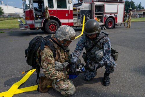 American and Japanese Airmen work together connecting a fire hose.