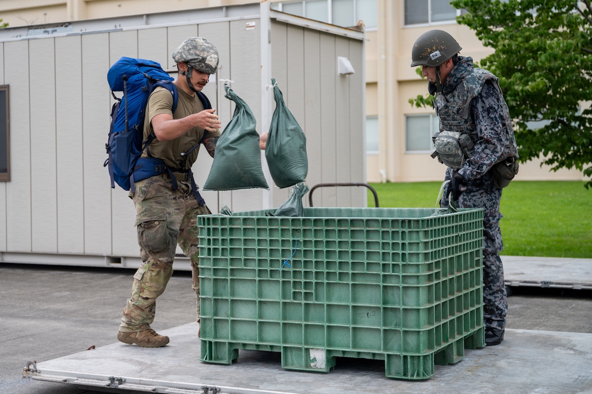 Airmen throw sandbags into a container.