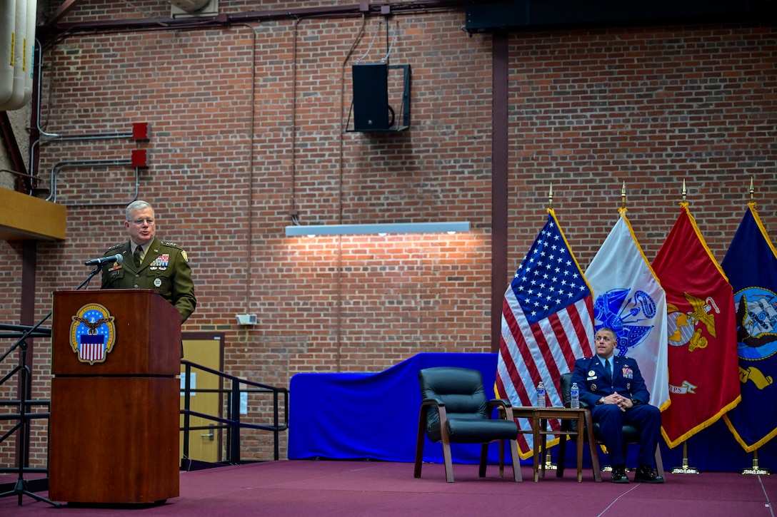 A three-star Army General standing on stage during a ceremony delivering opening remarks